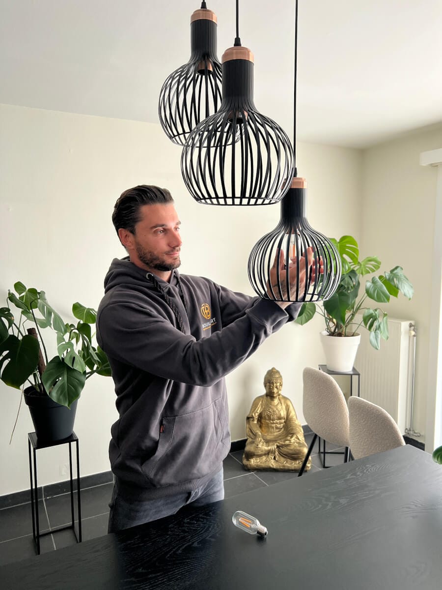 Elektricien Bouilliart die met oog voor detail een lamp installeert in een moderne hanglamp.